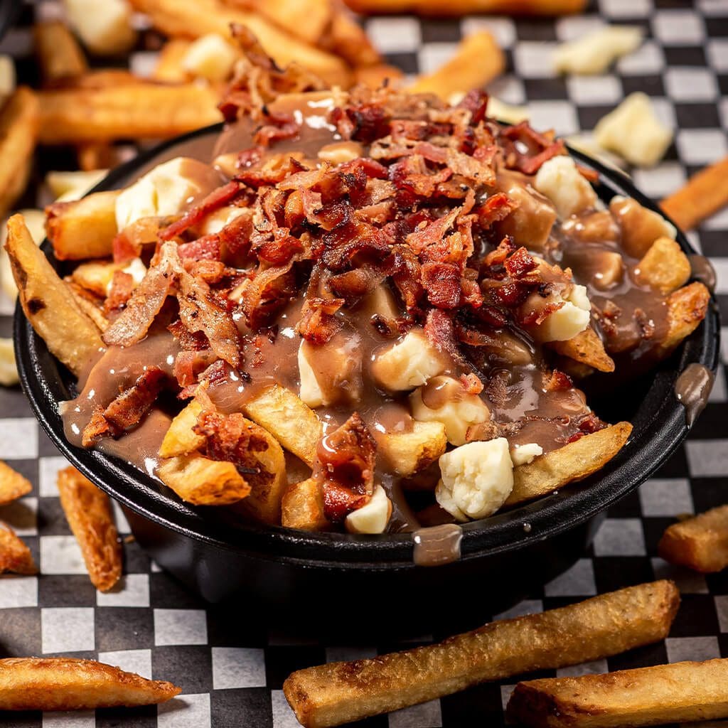 A bowl of bacon covered fries on top of a table.