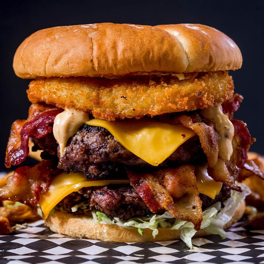 A large cheeseburger with fries and bacon on the side.